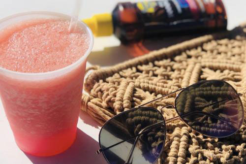 iced beverage next to sunglasses and tanning oil